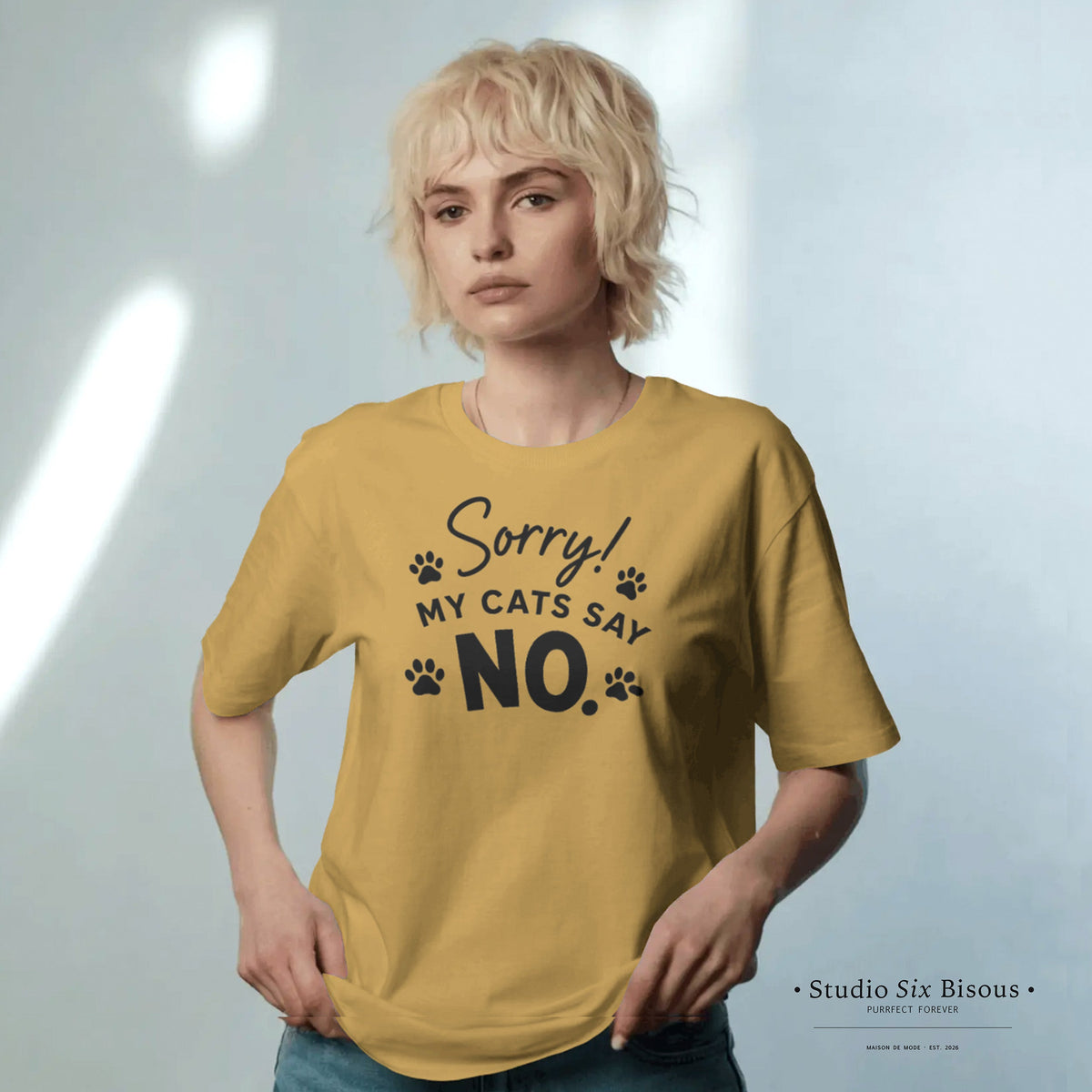 Model wearing a mustard yellow t-shirt with text 'Sorry! My cats say NO.' on a light gray background.