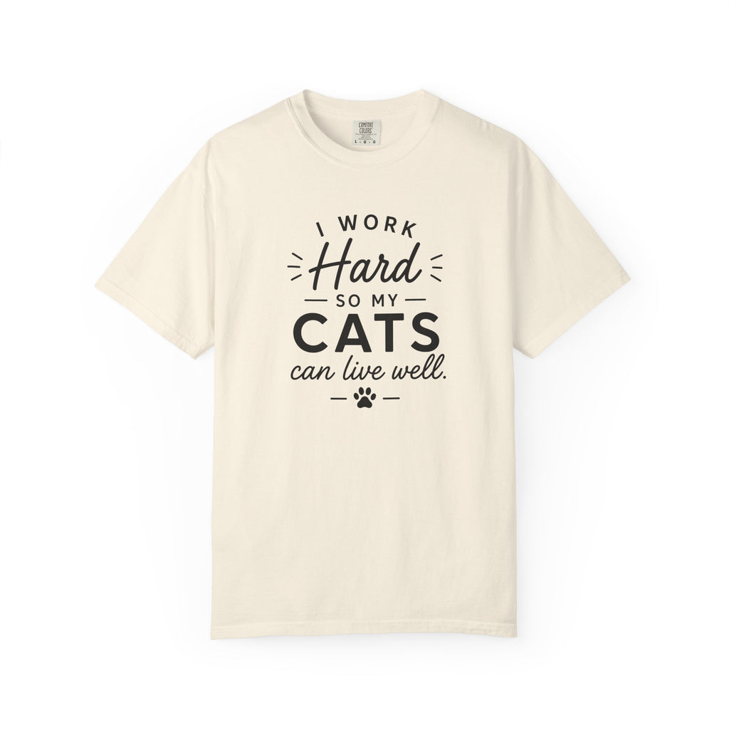 An off-white crewneck t-shirt with a black graphic text print that reads 'I WORK Hard SO MY CATS can live well.' with a paw print accent, displayed on a clean white background.