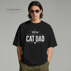 Person wearing a black t-shirt with 'Official Cat Dad 2026' text on a gray background