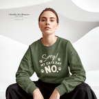 A woman wearing an olive green crewneck sweatshirt with the white printed text 'Sorry! MY CATS SAY NO.' and paw prints, seated against a white wavy studio background.