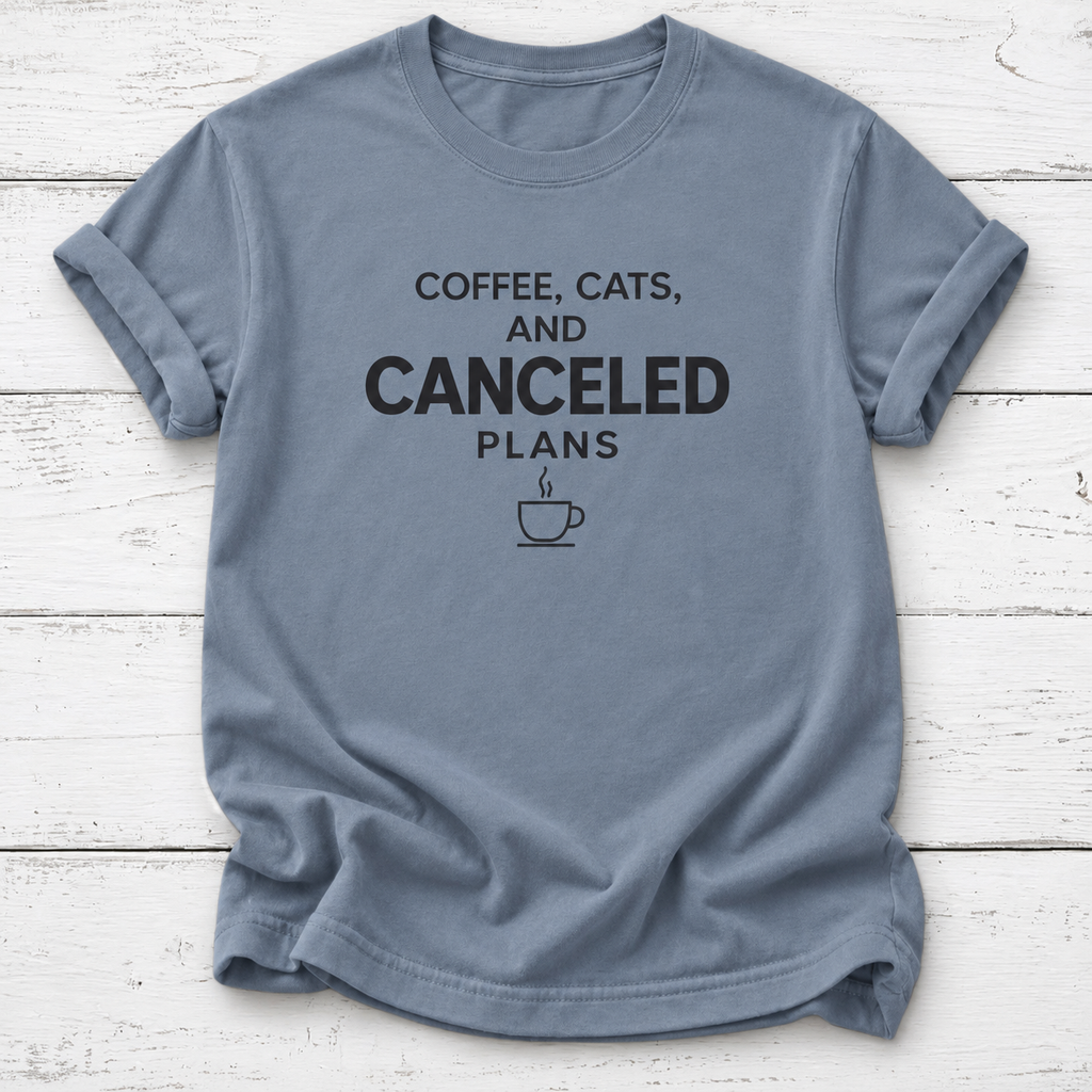 Slate blue T-shirt with black “Coffee, Cats, and Canceled Plans” lettering and a steaming coffee cup graphic, laid flat on white wooden boards.