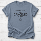 Slate blue T-shirt with black “Coffee, Cats, and Canceled Plans” lettering and a steaming coffee cup graphic, laid flat on white wooden boards.
