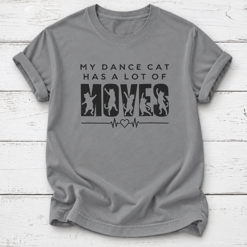 A gray short-sleeve crewneck t-shirt with a black graphic print that reads 'MY DANCE CAT HAS A LOT OF MOVES' with cat silhouettes inside the letters 'M-O-V-E-S' and a heartbeat line. The t-shirt is laid flat on a white wood plank background.
