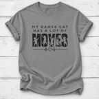 A gray short-sleeve crewneck t-shirt with a black graphic print that reads 'MY DANCE CAT HAS A LOT OF MOVES' with cat silhouettes inside the letters 'M-O-V-E-S' and a heartbeat line. The t-shirt is laid flat on a white wood plank background.