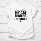 White T-shirt with black “I pay the bills, my cat makes the rules” lettering and a paw print, laid flat on white wooden boards.