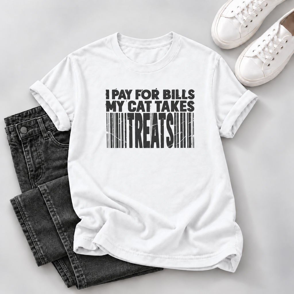 A white short-sleeve graphic T-shirt laid flat on a light gray surface, styled with folded dark gray jeans and white sneakers. The shirt has bold black text reading 'I PAY FOR BILLS MY CAT TAKES TREATS' above a barcode graphic.