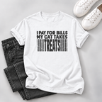 A white short-sleeve graphic T-shirt laid flat on a light gray surface, styled with folded dark gray jeans and white sneakers. The shirt has bold black text reading 'I PAY FOR BILLS MY CAT TAKES TREATS' above a barcode graphic.