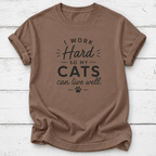 A brown crewneck t-shirt with a black graphic print that reads 'EST. 2026 OFFICIAL CAT DAD' with a paw print, laid flat on a white wood plank background.