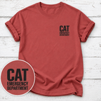 A terracotta red short-sleeve t-shirt with a black 'CAT EMERGENCY DEPARTMENT' text graphic on the left chest, displayed on a white wood background with a circular graphic overlay in the bottom left corner.