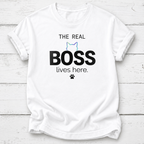 A white short-sleeve crewneck t-shirt laid flat on a white wood plank background. The shirt features a graphic print that reads 'THE REAL BOSS lives here.