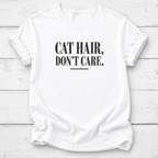 A white short-sleeve crewneck t-shirt with the text 'CAT HAIR, DON'T CARE.' printed in black serif font on the chest, laid flat on a white wood plank background.