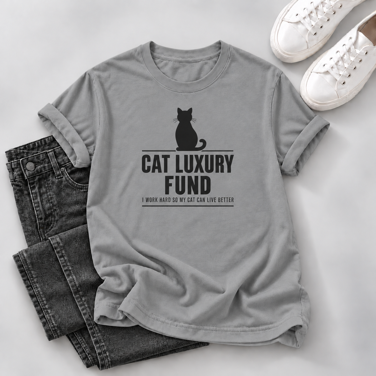 grey T-shirt with a white cat silhouette and “Cat Luxury Fund — I Work Hard So My Cat Can Live Better” lettering, laid flat on white wooden boards.