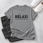 A gray short-sleeve T-shirt laid flat with rolled cuffs, featuring a black cat outline and the text 'RELAX! micro kneading treatment' on the front. The shirt is styled with folded dark jeans and white sneakers on a light gray background.