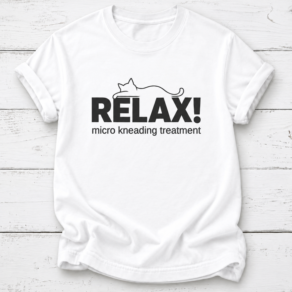 A white short-sleeve crewneck t-shirt with a black graphic print on the front. The graphic features the word 'RELAX!' in bold capital letters with a minimalist line drawing of a cat above it, and the phrase 'micro kneading treatment' printed below in a smaller font.