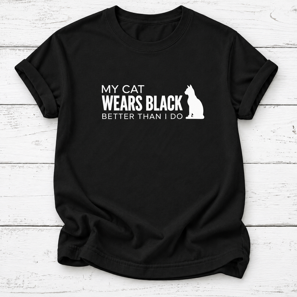 A black short-sleeve t-shirt with a white graphic print that reads 'MY CAT WEARS BLACK BETTER THAN I DO' alongside a white cat silhouette, displayed on a white wood plank background.