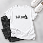 A white short-sleeve graphic T-shirt laid flat on a light gray surface, styled with folded dark gray jeans and white sneakers. The shirt has black text reading 'MY ORANGE CAT HAS A LOT TO SAY' with a soundwave graphic below.