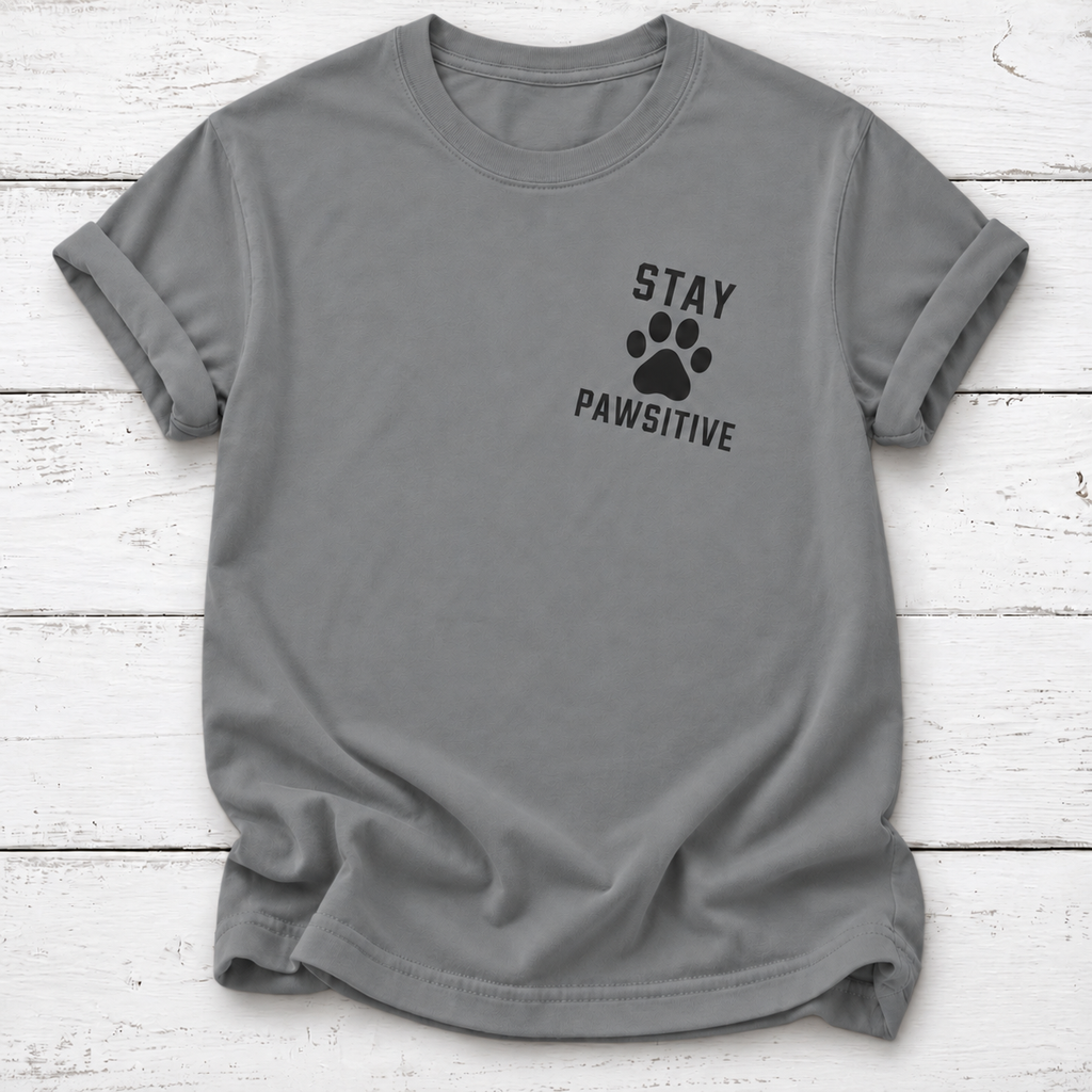 Gray T-shirt with a black paw print between “Stay” and “Pawsitive” on the left chest, with rolled sleeves, laid flat on white wooden board